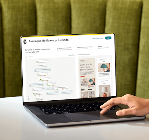 Imagem de uma pessoa sentada à mesa, olhando para a tela de um notebook que exibe o recurso de análise de jornada pronta para uso do Mailchimp. O recurso mostra uma prévia de uma jornada de automação e uma visão abstrata das interfaces de e-mail e SMS da marca fictícia Assembly. 